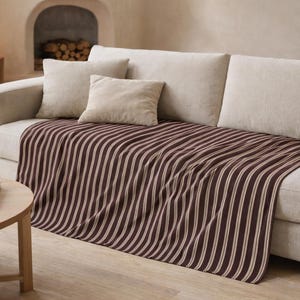 Puede incluir: Sof&aacute; crema con cojines beige y una manta a rayas marr&oacute;n y blanca. Una mesa de centro redonda de madera con una planta y una l&aacute;mpara est&aacute;n delante. La habitaci&oacute;n tiene una combinaci&oacute;n de colores neutros.