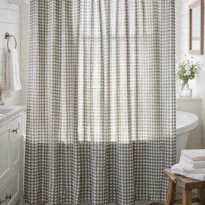 May include: A gray and white gingham shower curtain hangs in a bathroom. The curtain is hung from a curved rod and has a darker gray border at the bottom. The bathroom has white walls and a white vanity.
