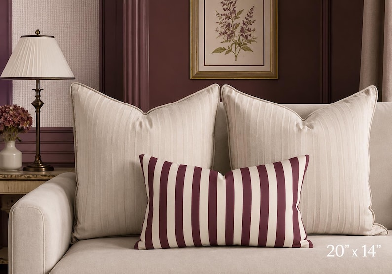 May include: Two large square throw pillows in a light beige fabric with a subtle vertical stripe pattern, paired with one smaller rectangular lumbar pillow featuring bold, vertical dark burgundy and beige stripes, measuring 20 inches by 14 inches.