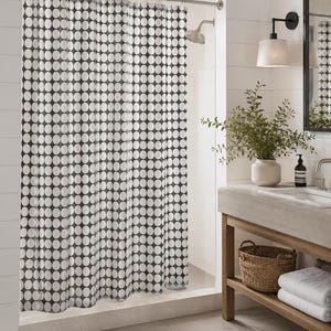 May include: A shower curtain featuring a repeating pattern of white circles on a dark gray background. The curtain hangs from a silver metal rod with integrated rings, creating vertical folds that extend from the top to the bottom edge.