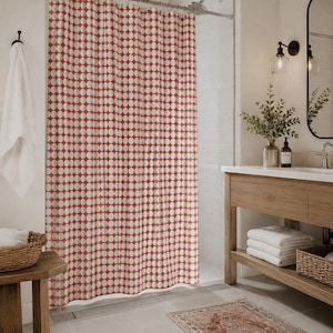 May include: A shower curtain featuring a repeating pattern of white circles on a terracotta red background. The curtain is suspended from a metal rod with rings and hangs in vertical folds, covering the shower area in a bathroom setting.