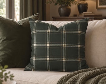 May include: A square throw pillow featuring a dark forest green fabric with a white and thin tan plaid pattern. The pillow is positioned upright, displaying a crisp, structured shape with clean edges and a consistent, repeating grid design.