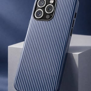 May include: A navy blue phone case with a vertical white stripe pattern. The case has a glossy finish and features a camera module with multiple lenses. The design is modern and sleek, offering protection and style.