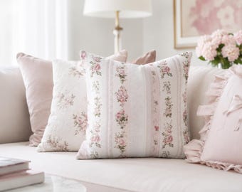 May include: A square throw pillow featuring a vertical striped pattern with alternating bands of pink roses on a white background and solid light pink stripes. The pillow has a soft fabric texture and is displayed alongside other decorative pillows.