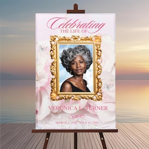 May include: A memorial sign on a wooden easel. The sign reads "Celebrating the Life of Veronica L. Turner" with a framed portrait of a woman. The background is a soft pink floral design with butterflies and a sunset.