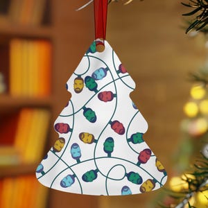 May include: A white Christmas tree-shaped ornament with a red ribbon. The ornament is decorated with a pattern of colourful Christmas lights. The lights are in various colours, including red, green, blue, and yellow.