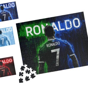 May include: A jigsaw puzzle featuring a back view of a football player wearing a jersey with the number 7 and the name RONALDO printed above it. The background displays the name RONALDO in large white letters with green and blue light effects.