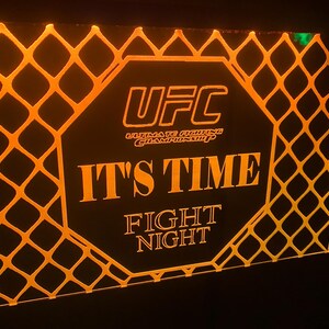 May include: A black and orange sign with the UFC logo and the text "It's Time Fight Night".