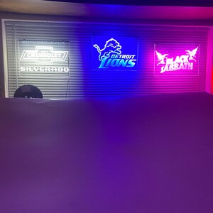 May include: Three illuminated signs with white text on a black background. The signs are lit with blue, purple, and red lights. The signs read "Chevrolet Silverado", "Detroit Lions", and "Black Sabbath".
