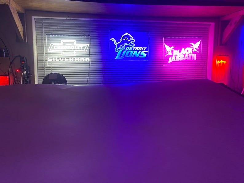May include: Three illuminated signs with white text on a black background. The signs are lit with blue, purple, and red lights. The signs read "Chevrolet Silverado", "Detroit Lions", and "Black Sabbath".