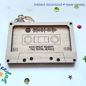 May include: A wooden cassette tape keychain with the text "SUCH GREAT HEIGHTS - THE POSTAL SERVICE" and a Spotify code. The keychain is light brown and has a metal keyring attached. The words "instant download &bull; laser-ready SVG file" are at the top.