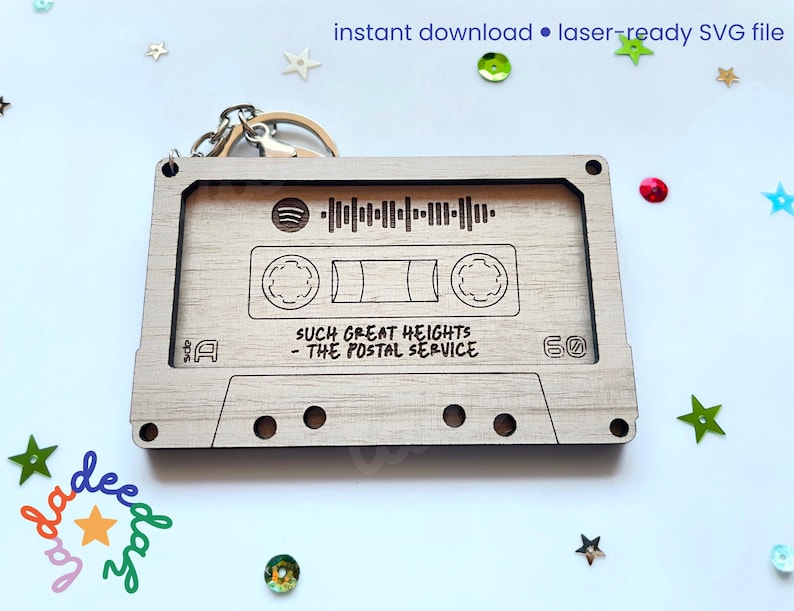May include: A wooden cassette tape keychain with the text "SUCH GREAT HEIGHTS - THE POSTAL SERVICE" and a Spotify code. The keychain is light brown and has a metal keyring attached. The words "instant download &bull; laser-ready SVG file" are at the top.