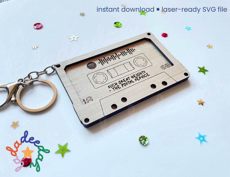 May include: A wooden cassette tape keychain with engraved details and a silver keyring. The keychain features the text "SUCH GREAT HEIGHTS - THE POSTAL SERVICE" and a soundwave graphic. The words "instant download &bull; laser-ready SVG file" are at the top.