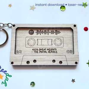 May include: A wooden cassette tape keychain with engraved details. The design includes a Spotify code, the text "SUCH GREAT HEIGHTS - THE POSTAL SERVICE", and a "60" marking. The keychain has a silver-colored ring and chain.