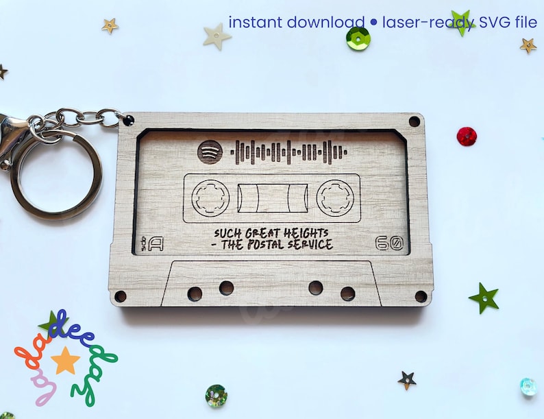 May include: A wooden cassette tape keychain with engraved details. The design includes a Spotify code, the text "SUCH GREAT HEIGHTS - THE POSTAL SERVICE", and a "60" marking. The keychain has a silver-colored ring and chain.