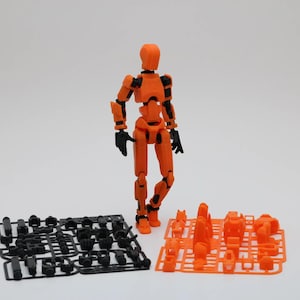 May include: An orange articulated action figure with black joints stands on a white surface. The figure is surrounded by two sets of black and orange plastic parts.