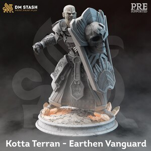 Puede incluir: Una miniatura gris de un guerrero impresa en 3D que sostiene un escudo con un diseño de calavera. La figura está de pie sobre una base redonda. El texto "Kotta Terran - Earthen Vanguard" está impreso debajo de la base.