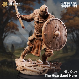 Puede incluir: Figura detallada de un guerrero vikingo, empuñando un hacha y un escudo. La figura está vestida con armadura y un casco, con detalles intrincados. El escudo es redondo y de madera. La base es un terreno rocoso. El texto dice "Shadow Over Nordheim" y "Nils Olav The Heartland Hero."