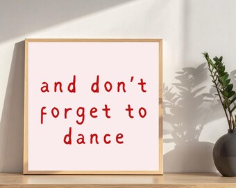 Può includere: Un'opera d'arte da parete quadrata incorniciata con uno sfondo rosa chiaro e il testo scritto a mano in rosso "and don't forget to dance" centrato sulla stampa. La cornice è in legno chiaro e ha un design semplice e lineare.