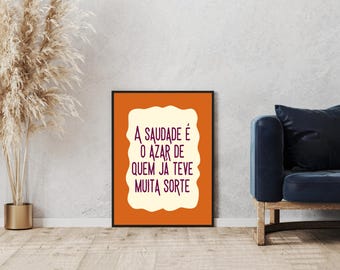 Può includere: Opera d'arte da parete incorniciata con testo portoghese in carattere viola su sfondo bianco sporco, su sfondo arancione. Il testo recita "A saudade é o azar de quem já teve muita sorte". L'opera è esposta in un soggiorno.