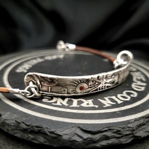 May include: Silver bracelet with a leather strap and a silver charm with a red stone and the year 1944 engraved on it.