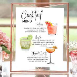 May include: A printable cocktail menu sign with watercolor illustrations of three cocktails: a Paloma, a Mojito, and an Aperol Spritz. The sign has a white background and is framed in a gold frame.