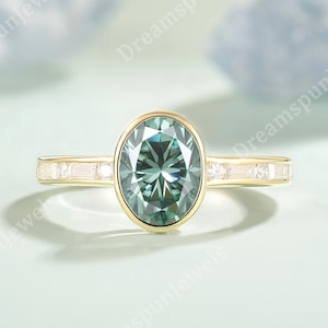 May include: A gold ring featuring an oval-cut, teal-colored gemstone. The band is accented with small, rectangular, clear gemstones. The ring has a classic, elegant design, suitable for engagement or special occasions.