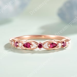 May include: Rose gold ring with alternating ruby and diamond detailing. The ring showcases marquise-cut rubies and small round diamonds in a repeating pattern. The ring is presented against a light blue backdrop.