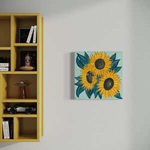 May include: A painting of three sunflowers with yellow petals and dark brown centres. The sunflowers are surrounded by dark blue leaves on a light blue background.