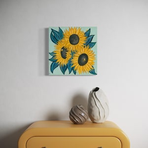 May include: A painting of three sunflowers with dark green leaves on a light blue background.