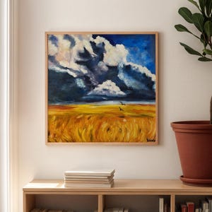 May include: Square framed painting depicting a wheat field under a dramatic sky. The sky is a mix of deep blue and white clouds, contrasting with the golden field. Two birds fly across the horizon. The painting is displayed above a bookshelf.