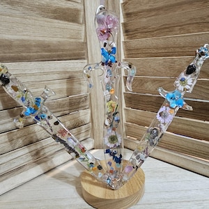 May include: Three clear resin dagger sculptures, each filled with dried flowers and small stones. The daggers are mounted on a wooden base. The flowers include blue, white, and purple blooms. The resin is clear, allowing the details of the flowers to be seen.