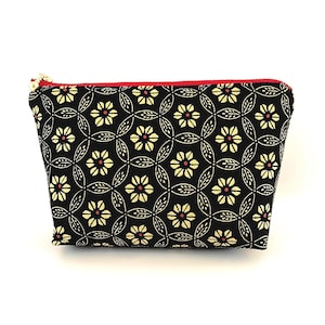 May include: Black cosmetic bag featuring a repeating floral design in yellow and red. The bag has a red zip and a gold-coloured zip pull. The bag is made of fabric and is likely used for storing makeup or toiletries.