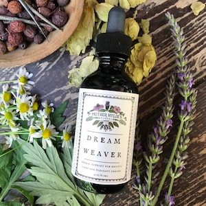 May include: A dark glass bottle with a white label that reads "MOTHER HYLDE'S HERBAL DREAM WEAVER HERBAL SUPPORT FOR RESTFUL SLEEP AND PLEASANT DREAMS 2 OZ/60 ML". The bottle is surrounded by dried flowers and herbs.