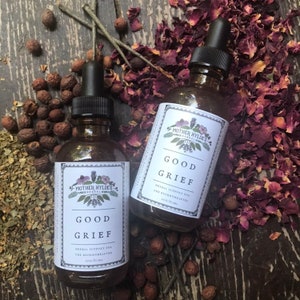Op de afbeelding: Twee bruine glazen flessen met zwarte druppelaars, met het opschrift "GOOD GRIEF" met bloemmotieven. De flessen zijn omgeven door gedroogde rozenblaadjes, bessen en kruiden, wat een natuurlijke apothekersesthetiek creëert. De tekst "HERBAL SUPPORT FOR THE BROKENHEARTED" is ook zichtbaar.
