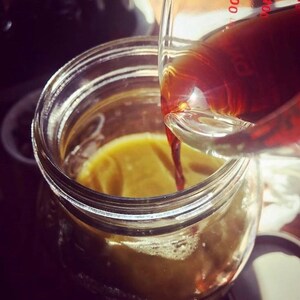 May include: A clear glass measuring cup pouring a dark liquid into a clear glass jar. The jar contains a yellow liquid. The image is a close-up shot, with the focus on the liquids and the glass containers.