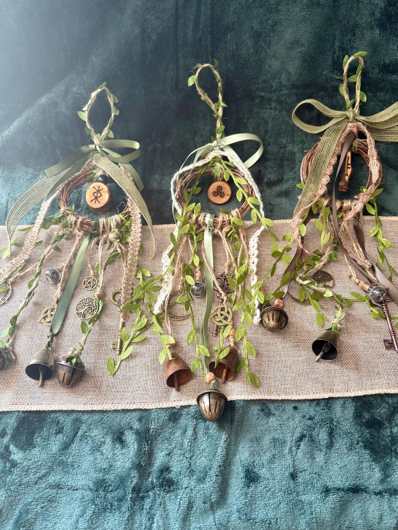 May include: Three hanging wall decorations featuring circular woven vine frames adorned with green faux ivy, jute twine, and olive green ribbons. Each piece includes dangling metal charms, keys, and bells, with small wooden discs displaying symbols.