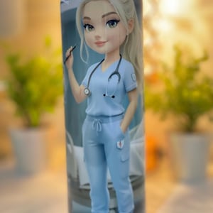 May include: A cylindrical tumbler featuring a cartoon illustration of a blonde nurse in light blue scrubs, holding a pen and stethoscope. The design includes a hospital bed in the background. The tumbler is designed for beverages.