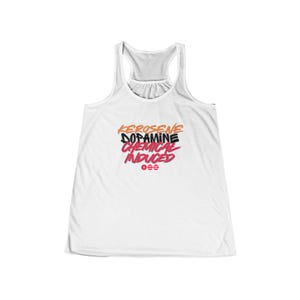 May include: White racerback tank top with the words "KEROSENE DOPAMINE CHEMICAL INDUCED" in orange, black, and red lettering. Below the text are three horizontal red circles. The tank top has a scoop neck and a racerback design.