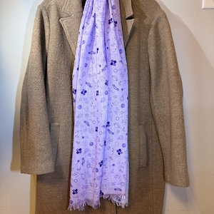 May include: A brown coat with a purple scarf featuring a pattern of various small white designs. The scarf is draped around the neck of the coat.
