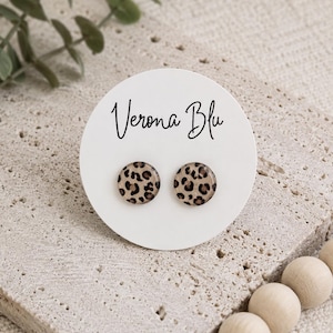 May include: A pair of round stud earrings featuring a tan and brown leopard print pattern. The earrings are attached to a circular white display card with the text Verona Blu printed in black script at the top center of the card.