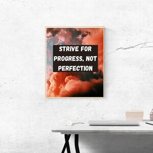 Puede incluir: Una cita motivacional, "Strive for progress, not perfection", impresa en blanco sobre un rectángulo negro, sobre un fondo de nubes rosas y naranjas.