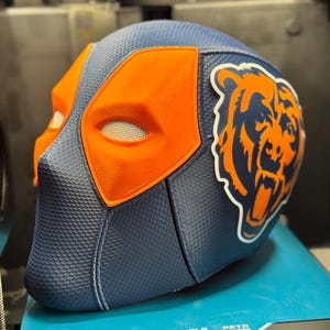 Könnte beinhalten: Eine 3D-gedruckte Maske in blau-orangener Farbgebung. Die Maske hat ein Bärenlogo an der Seite und eine Deadpool-artige Augenmaske auf der Vorderseite.