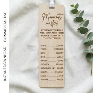 May include: A wooden bookmark with the words "Moments Matter" and a list of women from the Bible and their virtues. The bookmark has a white ribbon and is on a light-colored surface.