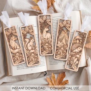 May include: Five rectangular wooden bookmarks featuring laser-cut designs of a fox, squirrel, deer, owl, and hedgehog surrounded by oak leaves and mushrooms. Each bookmark has a white fabric ribbon attached to the top and rests on an open book.