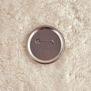 May include: The back of a round button with a silver pin and a gray backing.