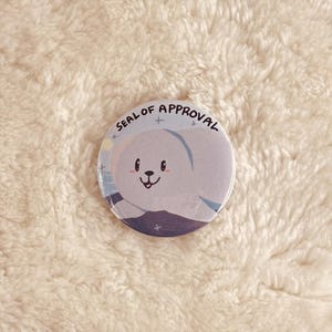 May include: A round button with a white seal of approval design. The seal features a cartoon seal with a blue and white background and the text "SEAL OF APPROVAL".