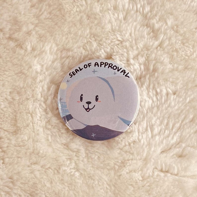 May include: A round button with a white seal of approval design. The seal features a cartoon seal with a blue and white background and the text "SEAL OF APPROVAL".