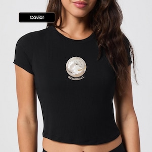 Puede incluir: Top corto negro acanalado con cuello redondo y mangas cortas. La camiseta presenta un gráfico de bola de discoteca plateada con la palabra "occasionally" debajo. La palabra "Caviar" está en un rectángulo negro en la esquina superior izquierda.