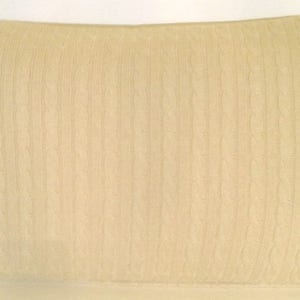 May include: A cream-colored knitted throw pillow with a cable knit pattern.
